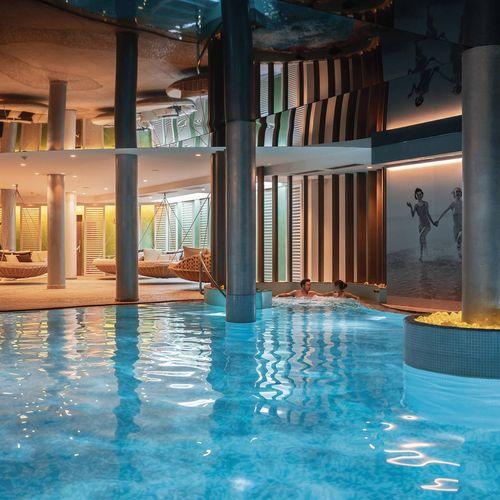 Ein heller Innenpool mit Liegen und warm beleuchtetem Spa-Bereich im Preidlhof.