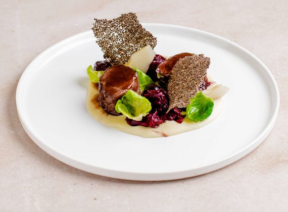 Ein angerichtetes Gourmetgericht auf einem weißen Teller mit Fleisch, Gemüse und knusprigen Chips.