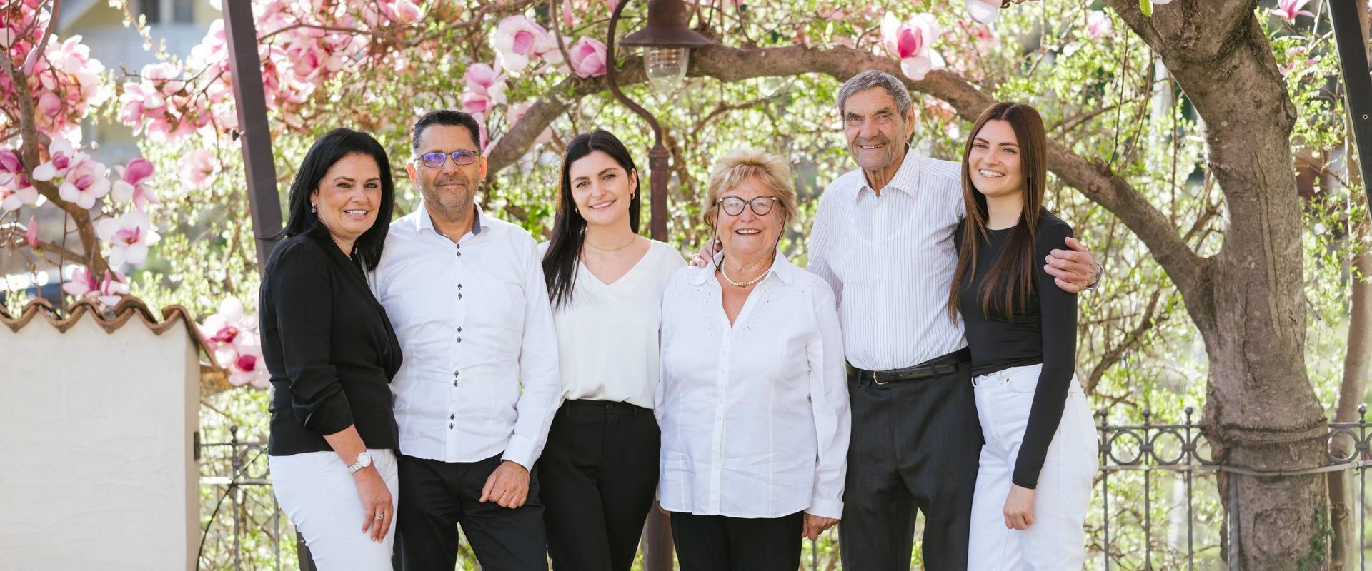 Die Familie Ladurner steht gemeinsam unter blühenden Frühlingsbäumen im Garten.