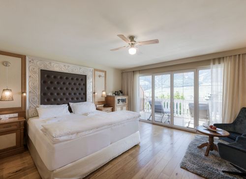Ein helles Schlafzimmer einer Luxussuite mit Doppelbett, Sitzbereich und Balkonfront mit Blick nach draußen.