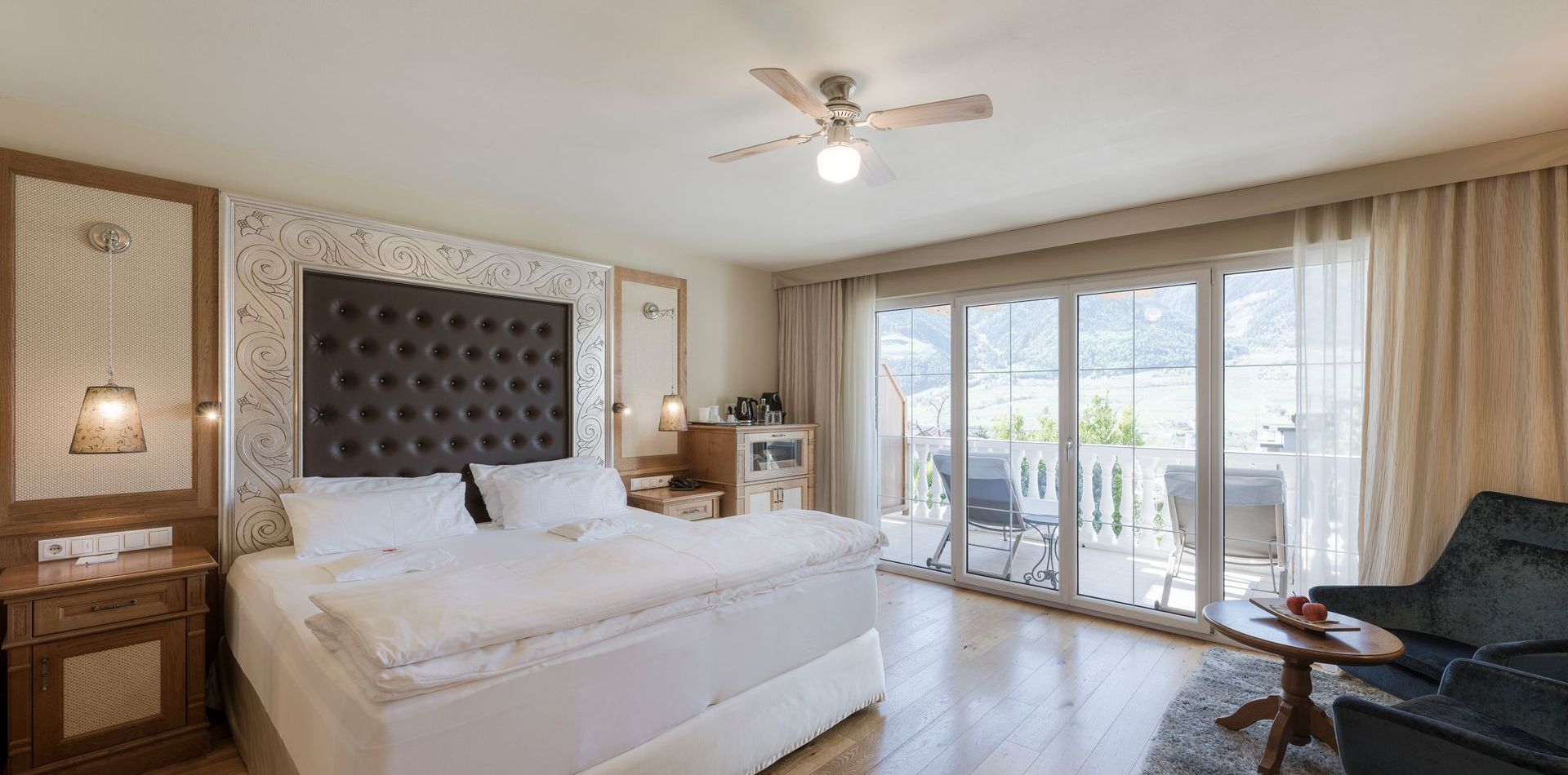 Ein helles Schlafzimmer einer Luxussuite mit Doppelbett, Sitzbereich und Balkonfront mit Blick nach draußen.