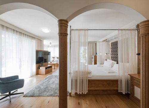Ein heller Schlafbereich mit Himmelbett, Vorhangdraperie und Holzmöbeln in einer Luxussuite.