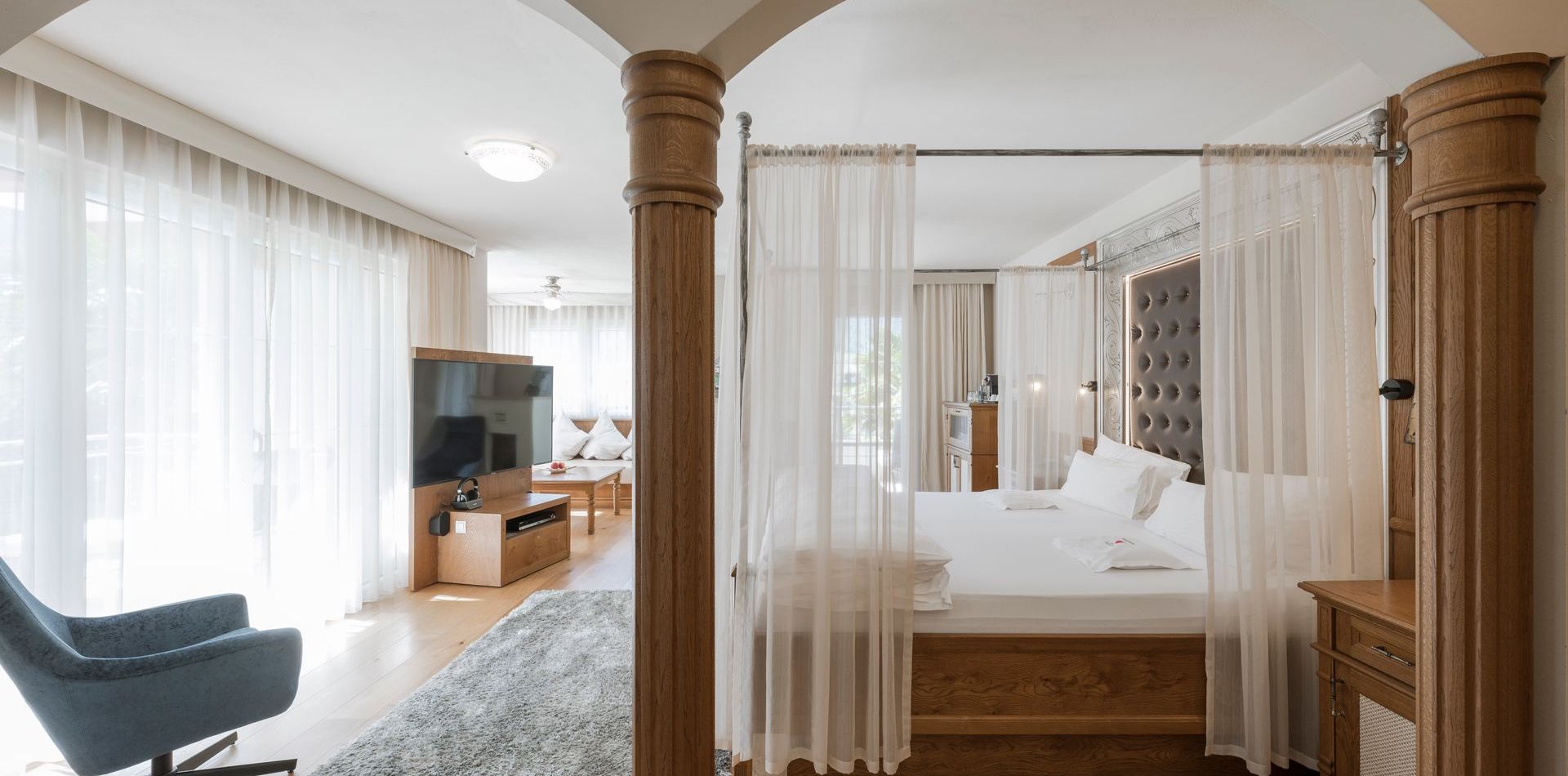 Ein heller Schlafbereich mit Himmelbett, Vorhangdraperie und Holzmöbeln in einer Luxussuite.