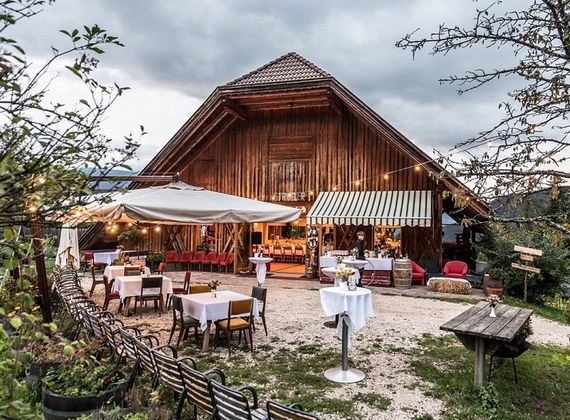 Vor einem hölzernen Haus stehen gedeckte Tische und Sonnenschirme im Gartenrestaurant.