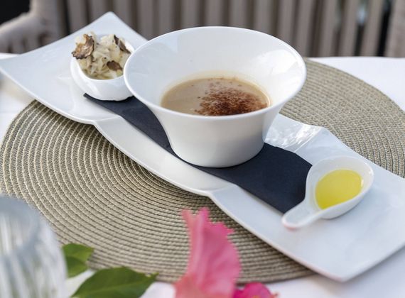 A plated dessert course with a small cup of cream, a white bowl of sauce and a yellow garnish on a woven placemat.