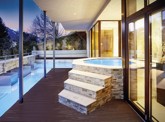 Ein Infinity-Pool und ein runder Whirlpool liegen auf einer überdachten Terrasse mit Blick in die Abenddämmerung.