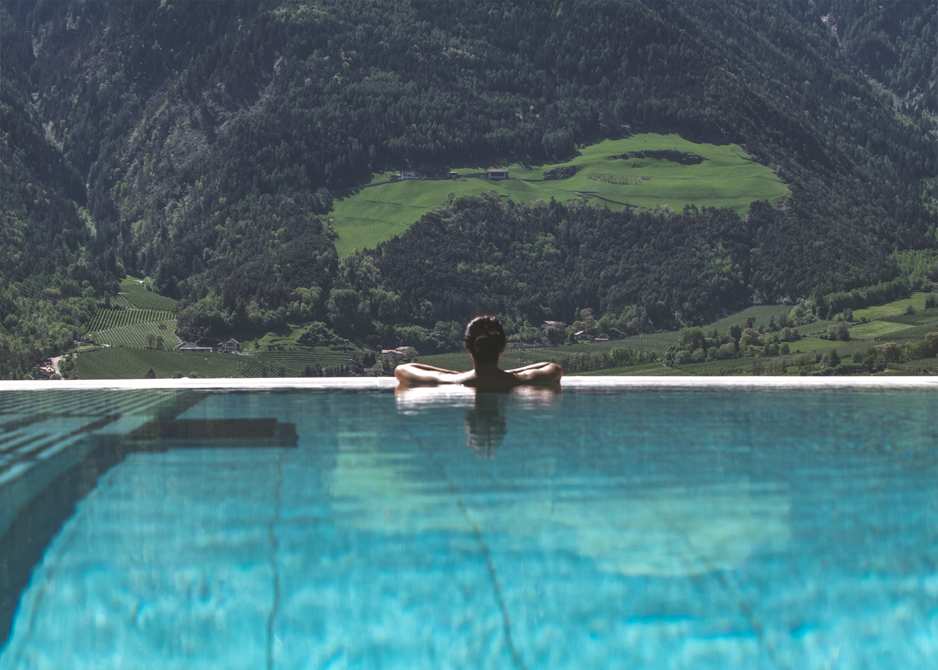 Una persona si rilassa sul bordo di una piscina a sfioro con le montagne sullo sfondo.